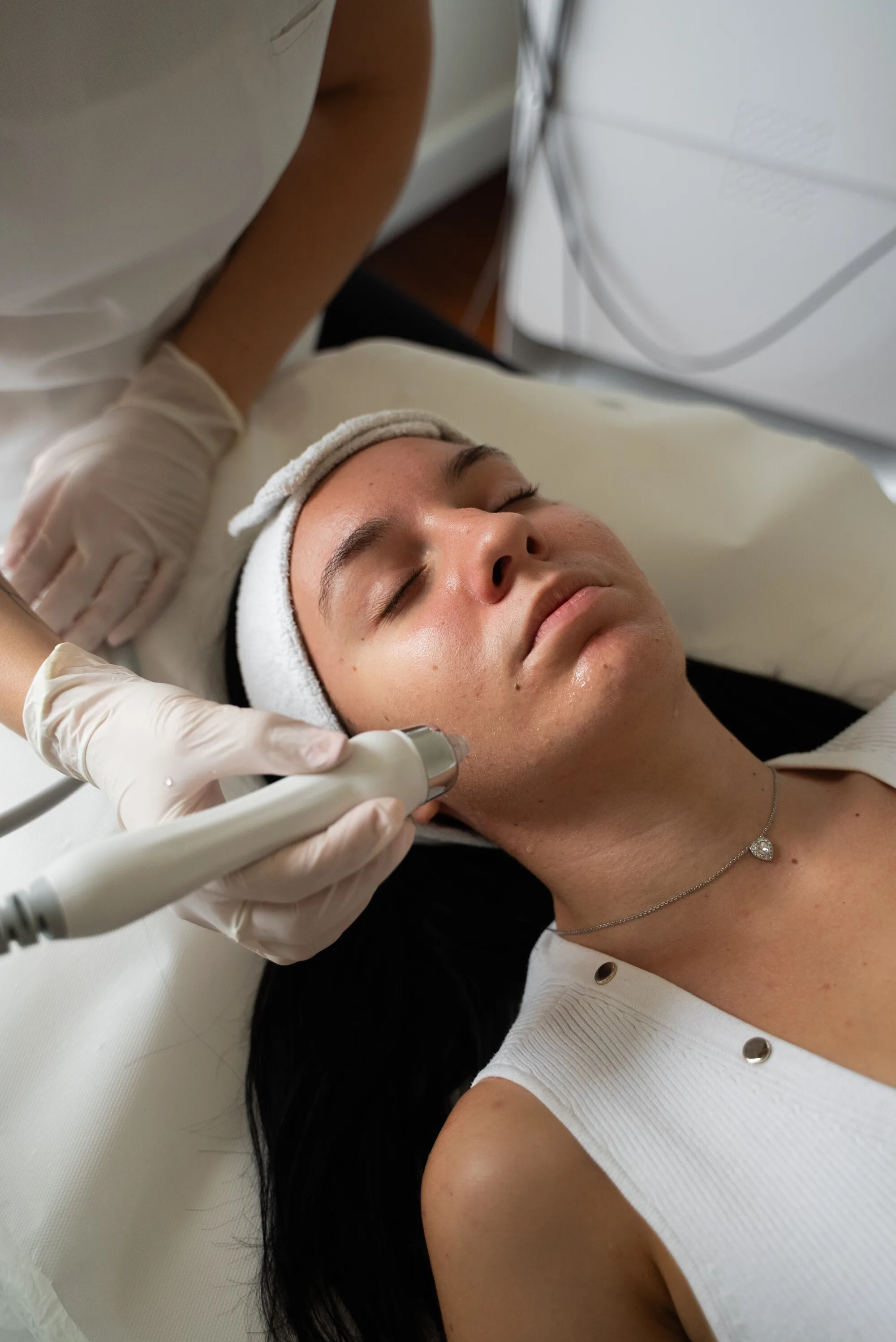 Tretman Hydrafacial7u1: nastavak uređaja na obrazu klijentice s bijelom trakom za kosu